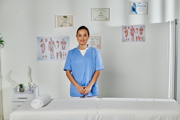 cheerful young female doctor in medical costume posing in her office and smiling at camera